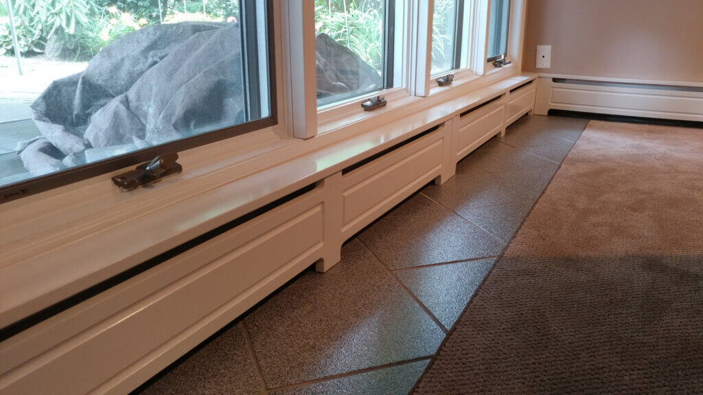 baseboard radiators covered with solid front baseboard covers painted while.  Installed under a window.